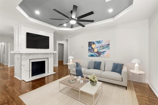 living room featuring a tray ceiling, ceiling fan, a fireplace, and hardwood / wood-style floors