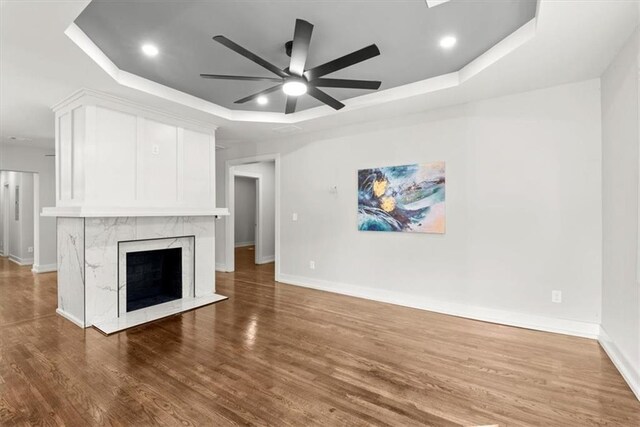 unfurnished living room featuring ceiling fan, dark hardwood / wood-style flooring, a raised ceiling, and a fireplace