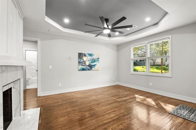 unfurnished living room with a fireplace, a raised ceiling, ceiling fan, and dark wood-type flooring