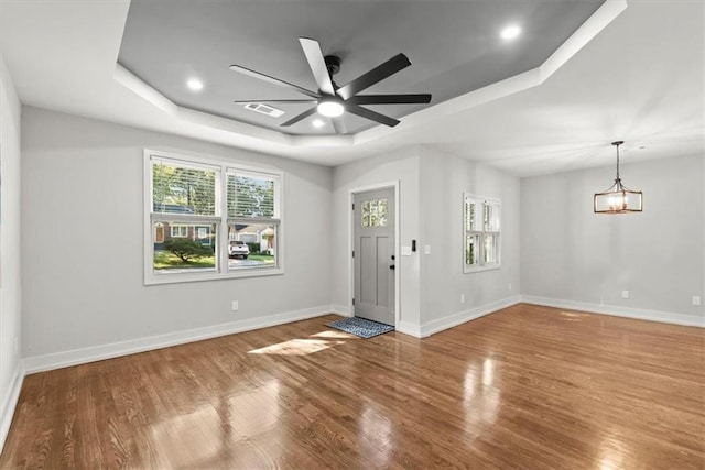 entrance foyer featuring hardwood / wood-style floors, ceiling fan with notable chandelier, and a tray ceiling