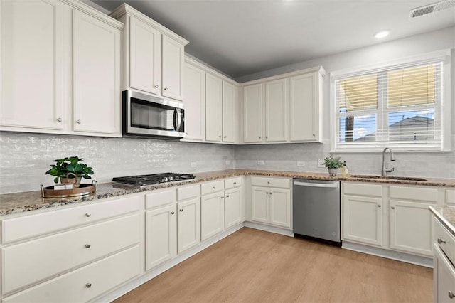 7410 Ansley View Ln, Cumming, GA 30028 - kitchen featuring appliances with stainless steel finishes, light wood-style flooring, white cabinetry, tasteful backsplash, and recessed lighting