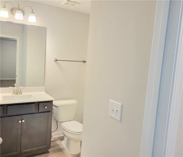 half bathroom featuring toilet, visible vents, wood finished floors, and vanity