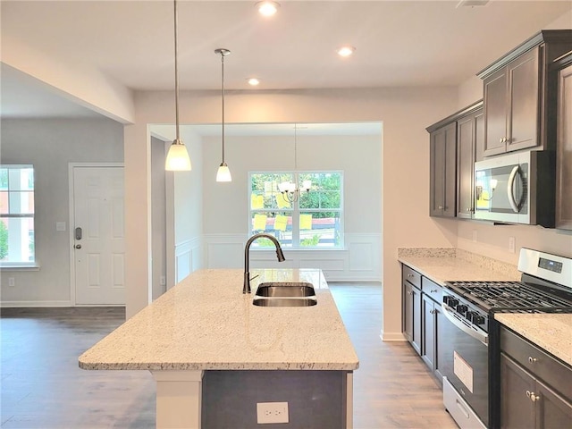 kitchen featuring stainless steel appliances, light stone counters, a sink, and a center island with sink