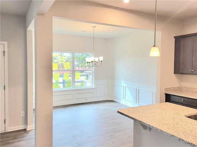 kitchen with light stone countertops, dark wood finished floors, dark brown cabinets, and decorative light fixtures