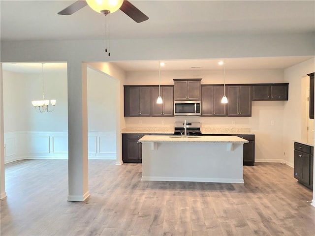 kitchen featuring a kitchen island with sink, stainless steel appliances, dark brown cabinets, light wood-style floors, and pendant lighting