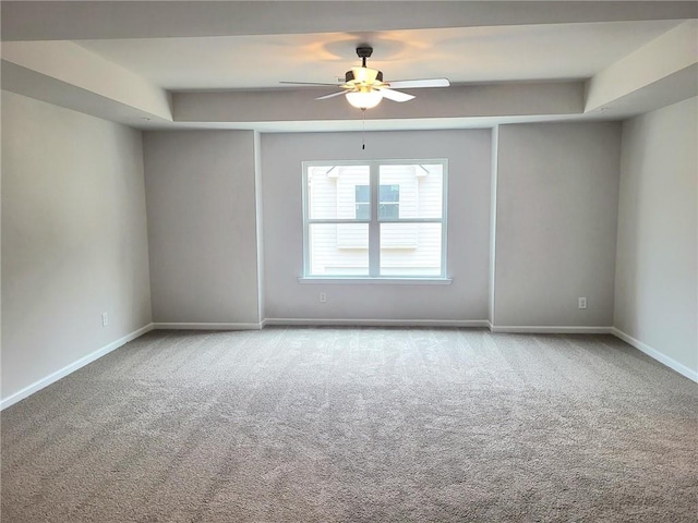 empty room with ceiling fan, baseboards, a raised ceiling, and light colored carpet