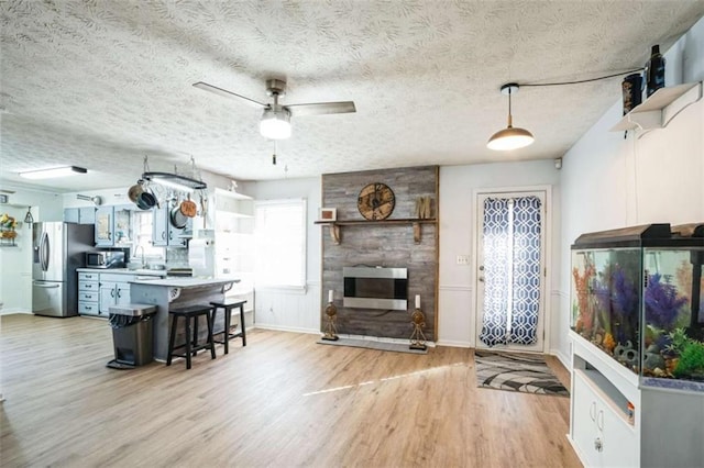 living room featuring a fireplace, sink, ceiling fan, light hardwood / wood-style floors, and a textured ceiling