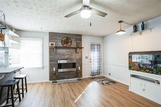 living room with ceiling fan, a fireplace, light hardwood / wood-style flooring, and a textured ceiling