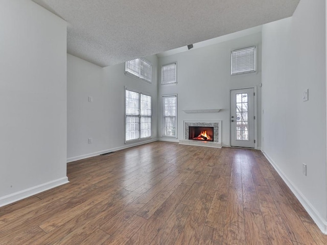 unfurnished living room with a tiled fireplace, hardwood / wood-style floors, a wealth of natural light, and a textured ceiling