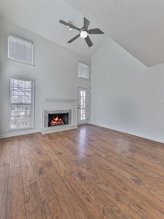 unfurnished living room with a tiled fireplace, hardwood / wood-style floors, high vaulted ceiling, and a textured ceiling