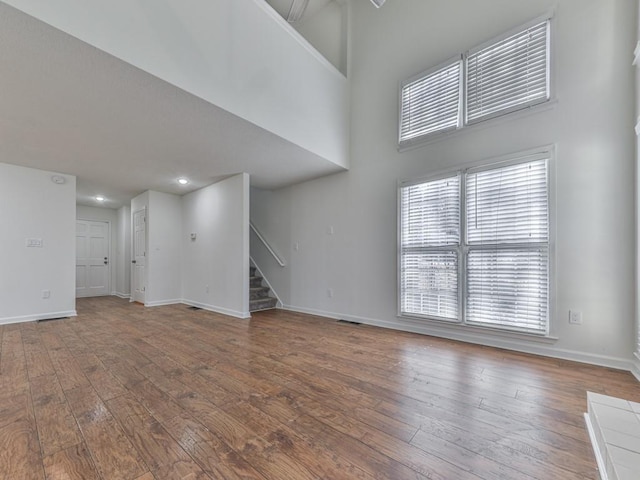 unfurnished living room with hardwood / wood-style flooring and a towering ceiling