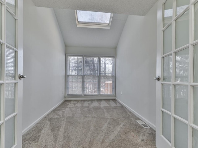 carpeted spare room featuring lofted ceiling with skylight