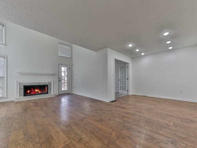 unfurnished living room featuring a tiled fireplace, wood-type flooring, and a textured ceiling