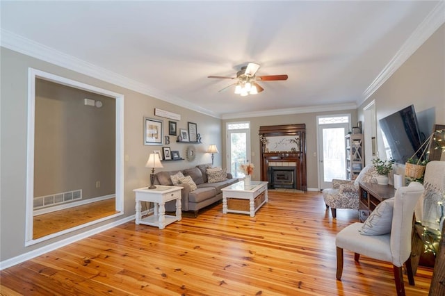 living area with a fireplace, light wood finished floors, visible vents, ornamental molding, and a ceiling fan