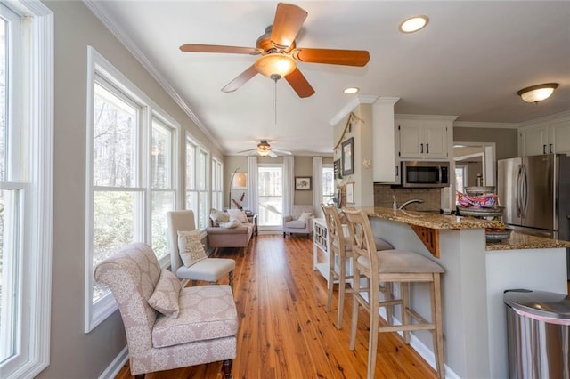 kitchen featuring light stone counters, a peninsula, white cabinets, ornamental molding, and appliances with stainless steel finishes