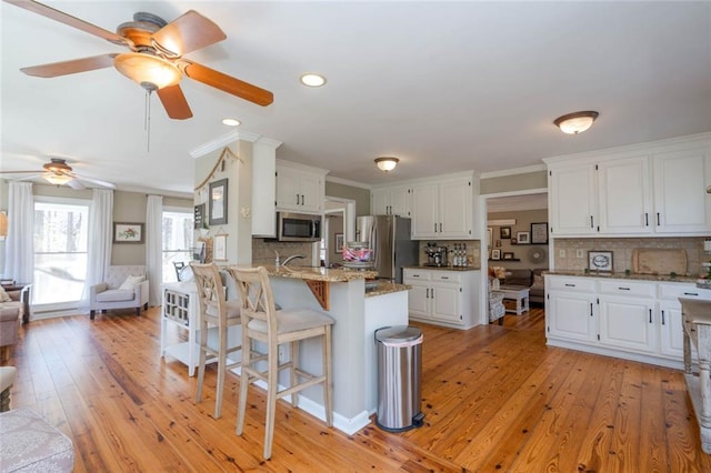 kitchen with a breakfast bar area, light wood finished floors, stainless steel appliances, open floor plan, and white cabinets