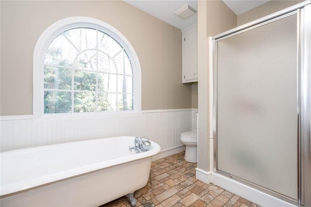 full bathroom featuring a freestanding tub, toilet, a wainscoted wall, visible vents, and a shower stall