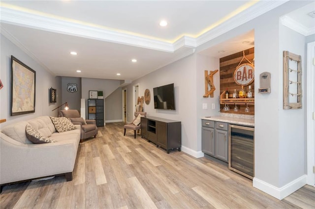 living area with wine cooler, baseboards, light wood-style floors, ornamental molding, and a dry bar