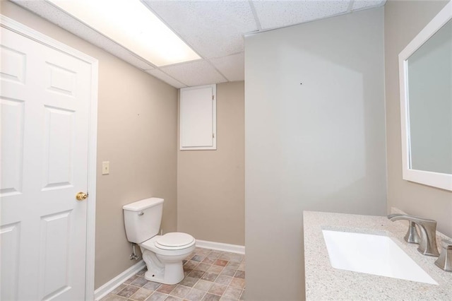 half bath featuring toilet, a paneled ceiling, baseboards, and a sink