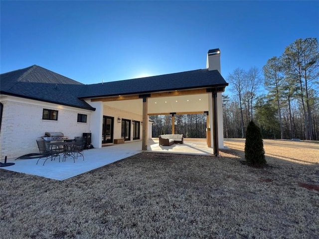 back of property with a shingled roof, outdoor lounge area, a patio, and a chimney