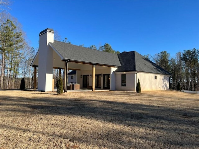 back of property with a shingled roof, a lawn, a chimney, and stucco siding