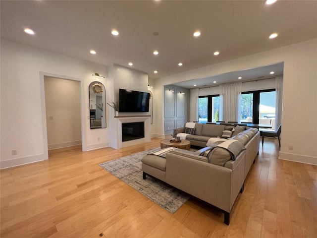 living area with light wood-type flooring, a glass covered fireplace, baseboards, and recessed lighting