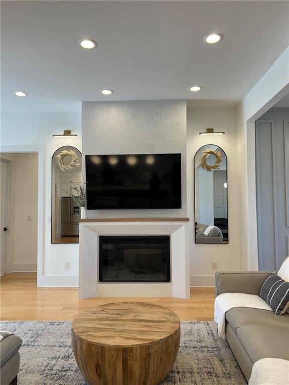 living area with a glass covered fireplace, baseboards, recessed lighting, and wood finished floors