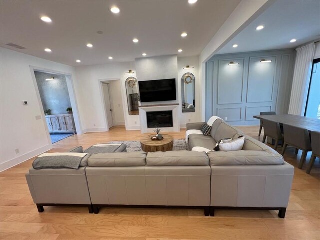 living area featuring visible vents, baseboards, light wood-style floors, a fireplace, and recessed lighting