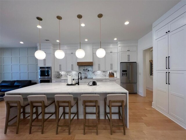 kitchen with hanging light fixtures, appliances with stainless steel finishes, a large island, and light stone counters