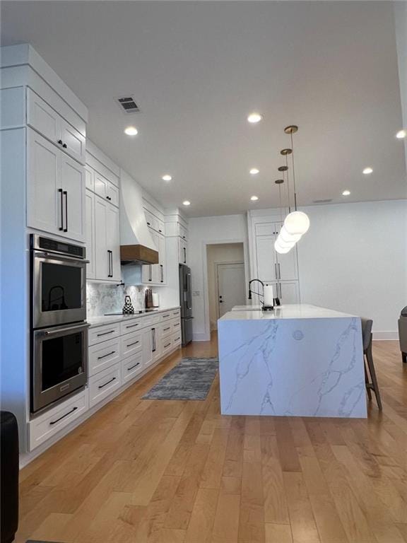 kitchen featuring custom range hood, white cabinets, and a center island with sink