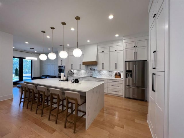 kitchen with white cabinets, a large island, appliances with stainless steel finishes, decorative light fixtures, and premium range hood