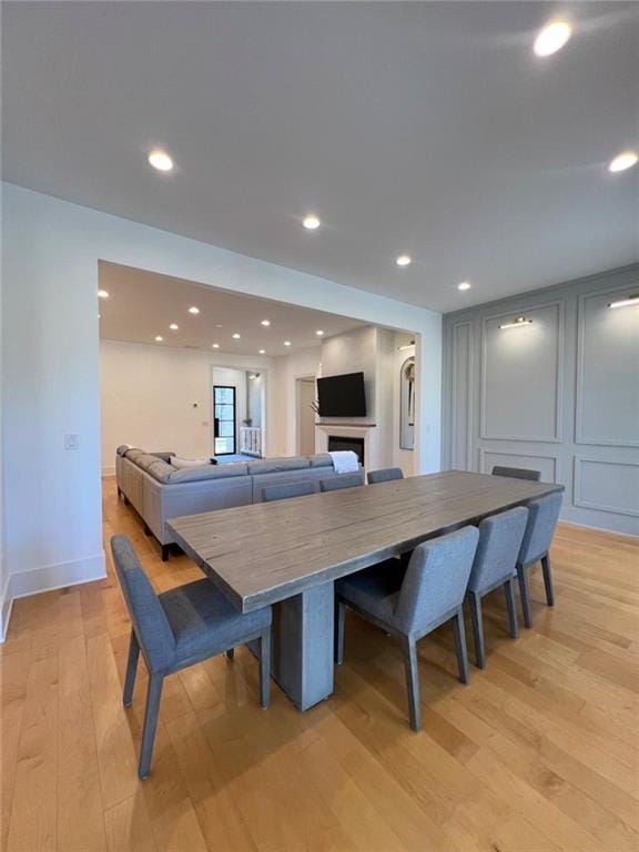 dining space featuring light wood-type flooring, a decorative wall, a fireplace, and recessed lighting