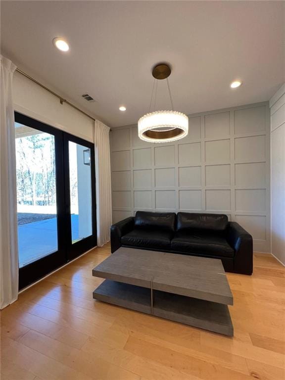 living room with light wood-style floors, french doors, visible vents, and a decorative wall