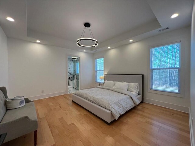 bedroom with a tray ceiling, light wood-style flooring, visible vents, and recessed lighting