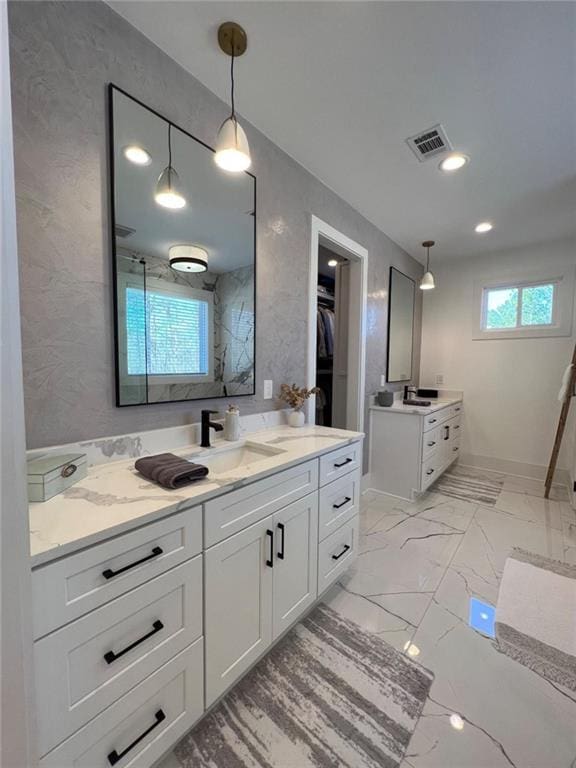 bathroom featuring visible vents, a sink, marble finish floor, a walk in closet, and two vanities