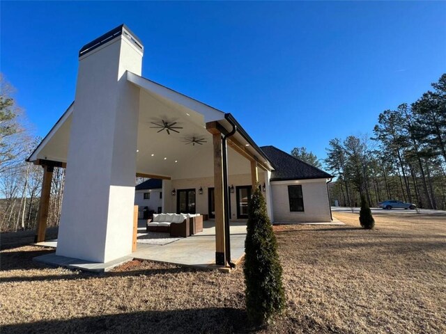 rear view of property with a ceiling fan, a chimney, an outdoor hangout area, a patio area, and stucco siding
