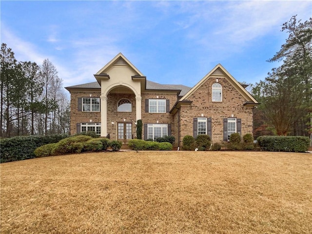 view of front of house with french doors, brick siding, and a front yard