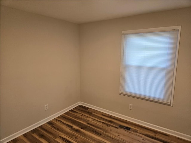 empty room with dark wood-type flooring, visible vents, and baseboards