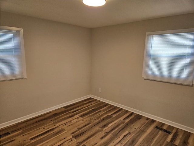 spare room featuring visible vents, dark wood finished floors, and baseboards