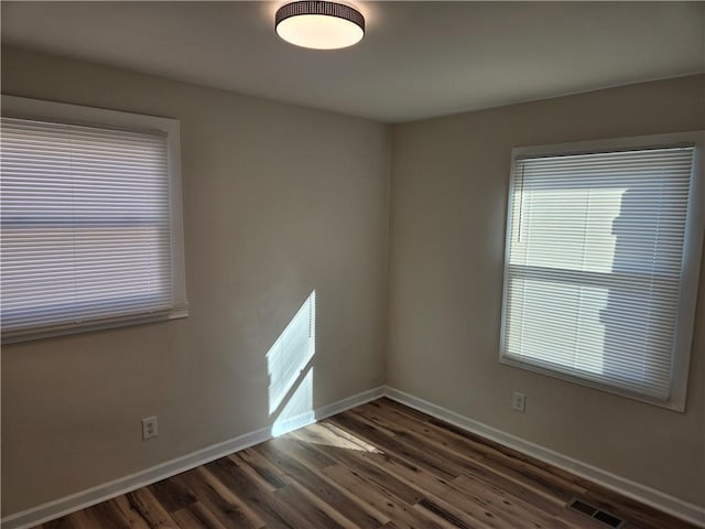 spare room with dark wood-style flooring, visible vents, and baseboards