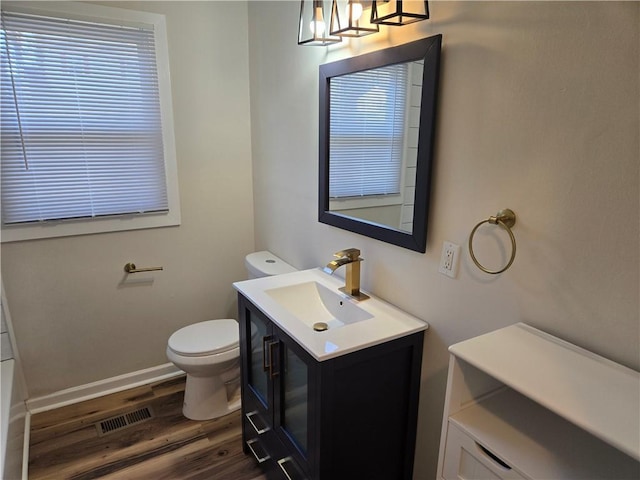 bathroom with toilet, wood finished floors, vanity, visible vents, and baseboards