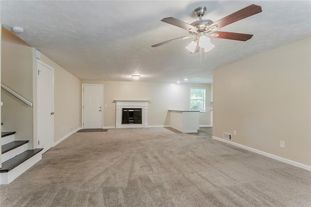unfurnished living room featuring carpet, stairway, baseboards, ceiling fan, and a textured ceiling