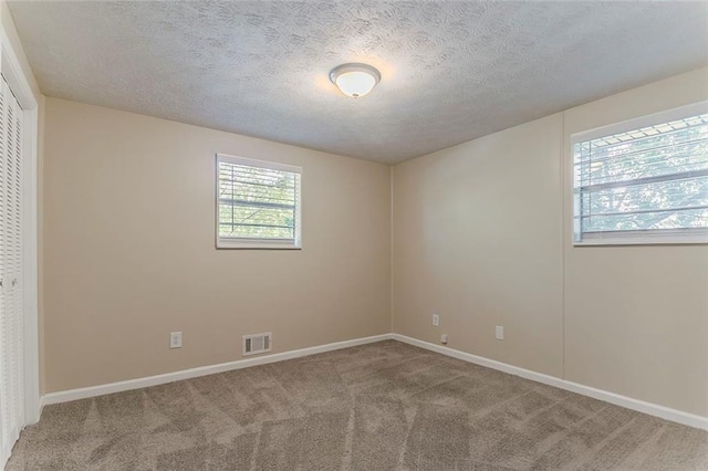 carpeted empty room featuring a textured ceiling and baseboards