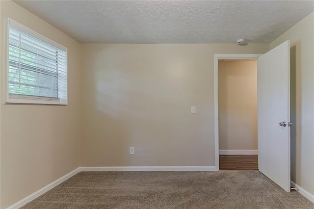 spare room featuring carpet floors, a smoke detector, baseboards, and a textured ceiling