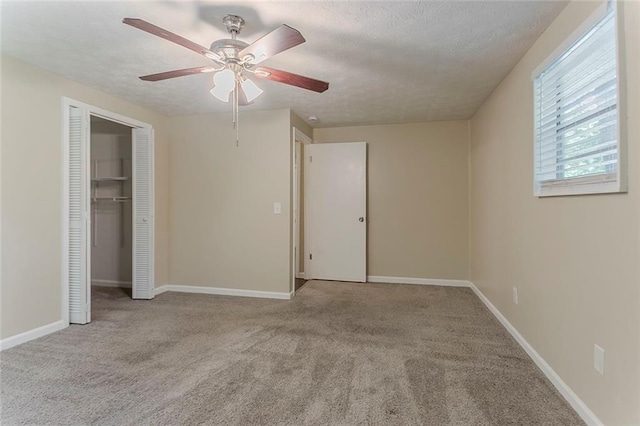 unfurnished bedroom with a textured ceiling, carpet, a closet, ceiling fan, and baseboards