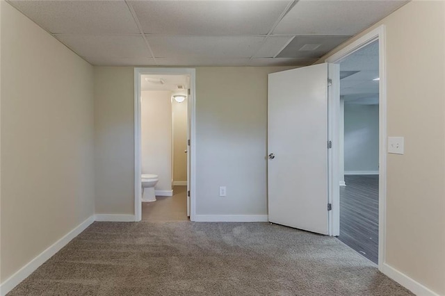 unfurnished bedroom featuring a drop ceiling, carpet flooring, a walk in closet, and baseboards