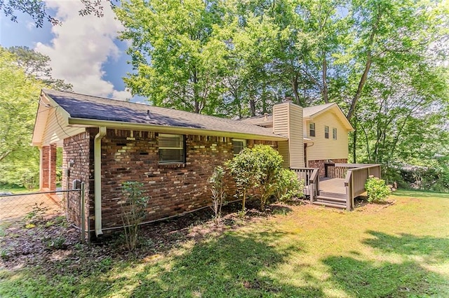 rear view of house featuring brick siding, a lawn, a wooden deck, a chimney, and roof with shingles