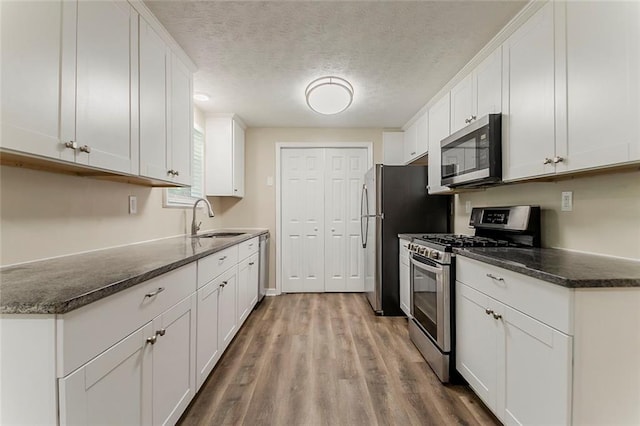 kitchen featuring appliances with stainless steel finishes, a sink, white cabinets, wood finished floors, and a textured ceiling