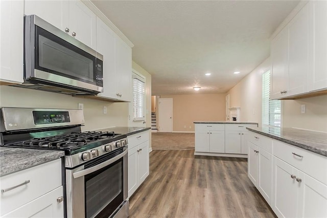 kitchen featuring appliances with stainless steel finishes, white cabinetry, recessed lighting, wood finished floors, and stone counters