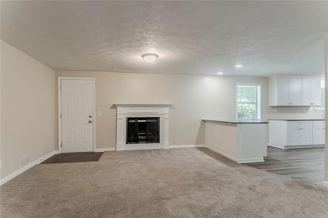 unfurnished living room featuring carpet, a fireplace, a textured ceiling, and baseboards